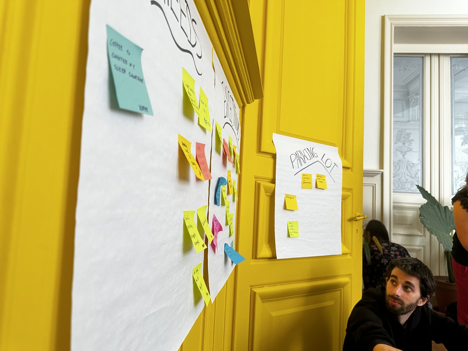 Jan from Eleven Ways looking at a white board with sticky notes on it. The words 'needs', 'expectations' and 'parking lot' are visible.